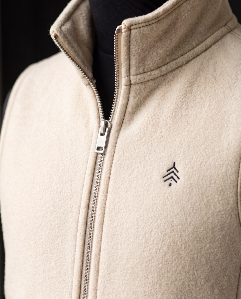 A close view of a cream Cedar Rowe fleece, its collar, zip pull and the cedar mark.
